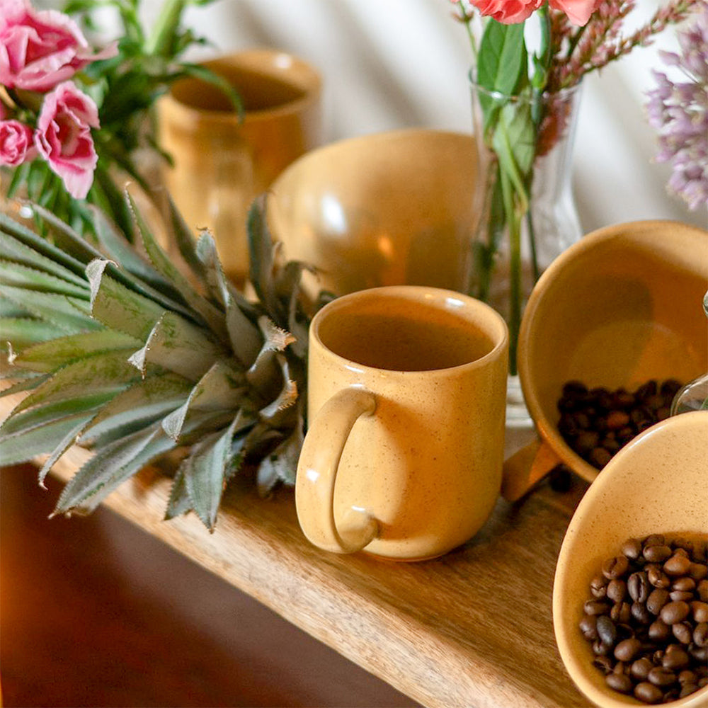 Set of ceramic mugs and bowls on a wooden surface with flowers and a pineapple.